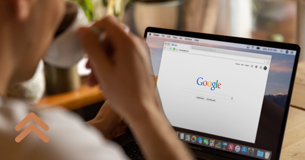 Onderneemster met een kop koffie aan een houten tafel, met de startpagina van Google open op haar laptop en het BusinessBoosters-logo linksonder
